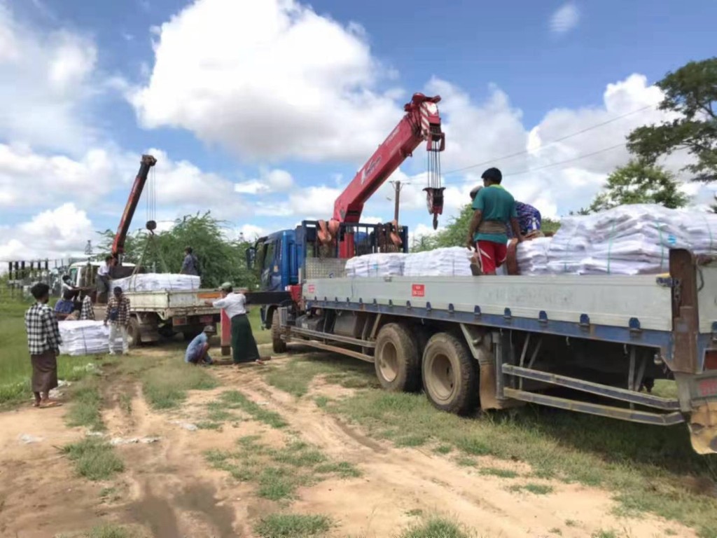 Workers and crane trucks loading white sacks onto flatbed lorries
